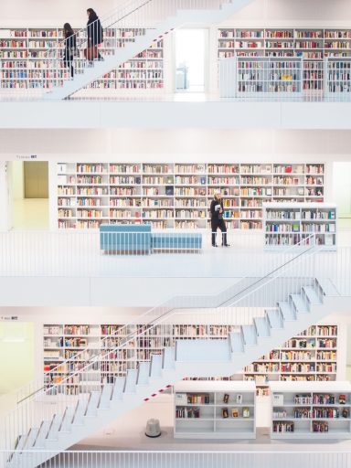 Zwei Personen auf Treppen in einer modernen Bibliothek mit Regalen voller Bücher.