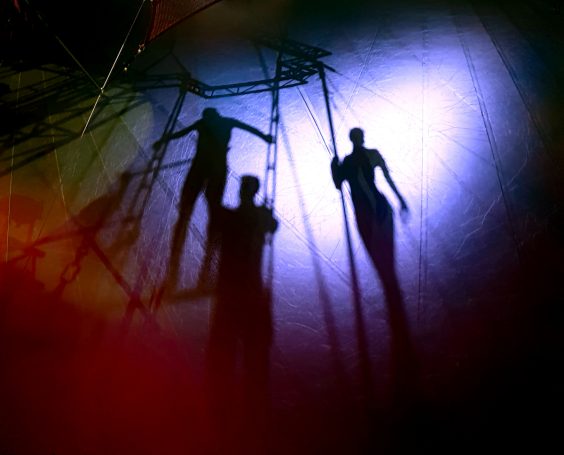 Schatten von drei Figuren, beleuchtet in lila und orange, auf einer strukturierten Oberfläche.