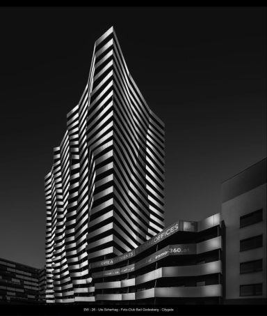 Moderne, gewundene Hochhausfassade in schwarz-weiß, gegen einen dunklen Himmel.