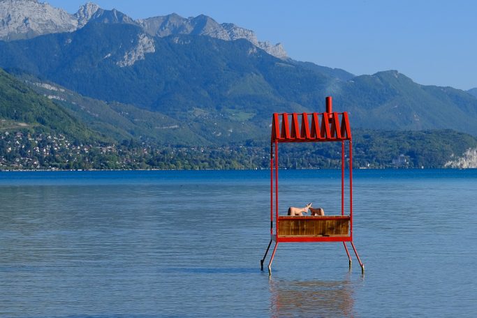 Rotes Gestell im flachen Wasser, umgeben von Bergen und klarem Himmel.