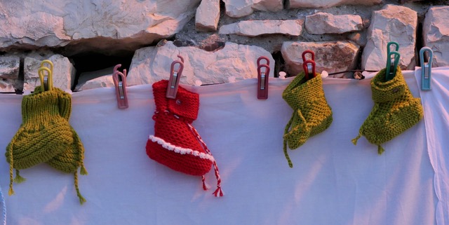 Kleine Füßchen Bunte Strümpfe hängen an einer Wäscheleine vor einer steinigen Wand.