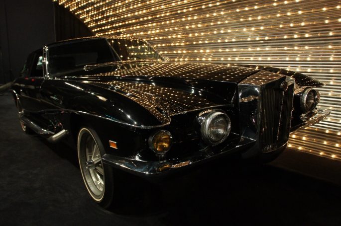 Ein schwarzer Luxuswagen mit glänzendem Finish vor einer Lichterwand.