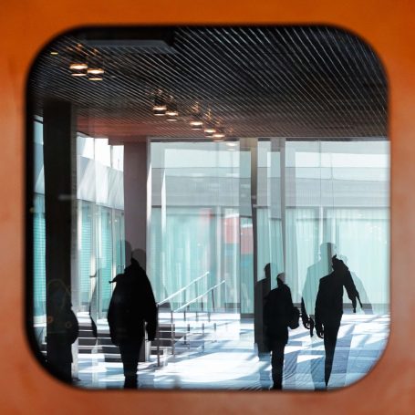 Silhouetten von Personen, die durch ein Fenster in einem modernen Gebäude gehen.