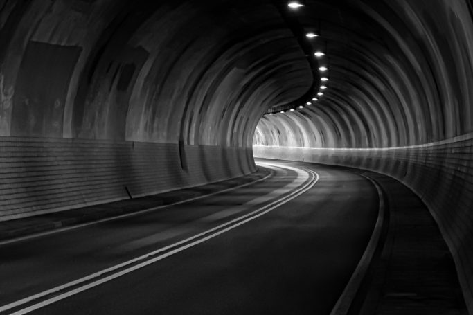 Kurvenreicher Tunnel mit beleuchteten Wänden und Straße in Schwarzweiß.