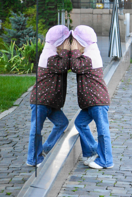 Kind in der Ukraine 2011 Ein Kind mit Kopftuch spiegelt sich in einer Wasserpfütze und sieht zwei von sich selbst.