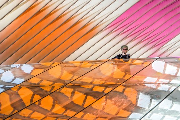 Junge steht auf einem Balkon mit bunten, geometrischen Wänden aus orangefarbenen und rosa Farbtönen.